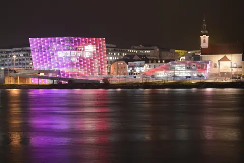 Das Ars Electronica Center in Linz leuchtet nachts violett über der Donau